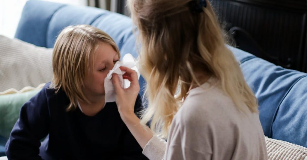 A mother tends to her sick child with a tissue on the couch, showcasing care and comfort.